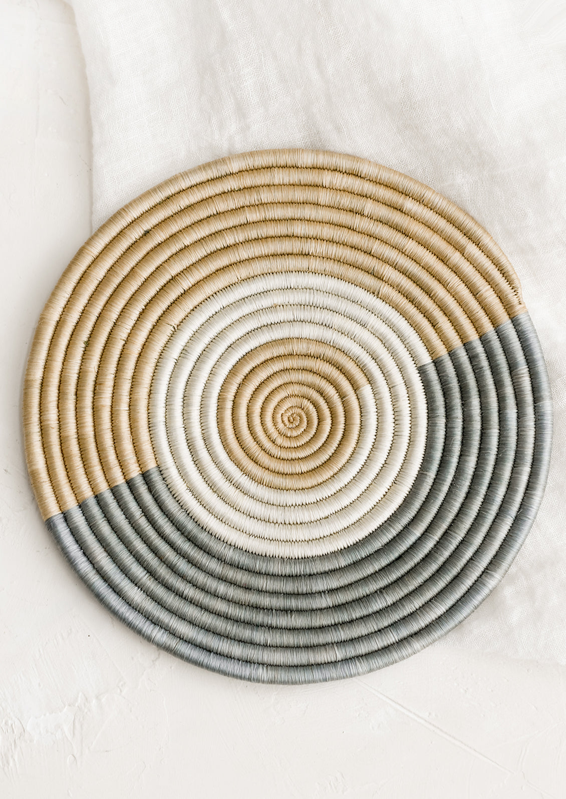 A woven trivet in tan and dusty blue.