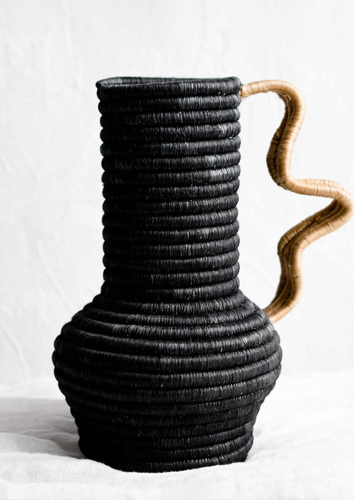 A sculptural sweetgrass vase with wavy handle in black with tan.
