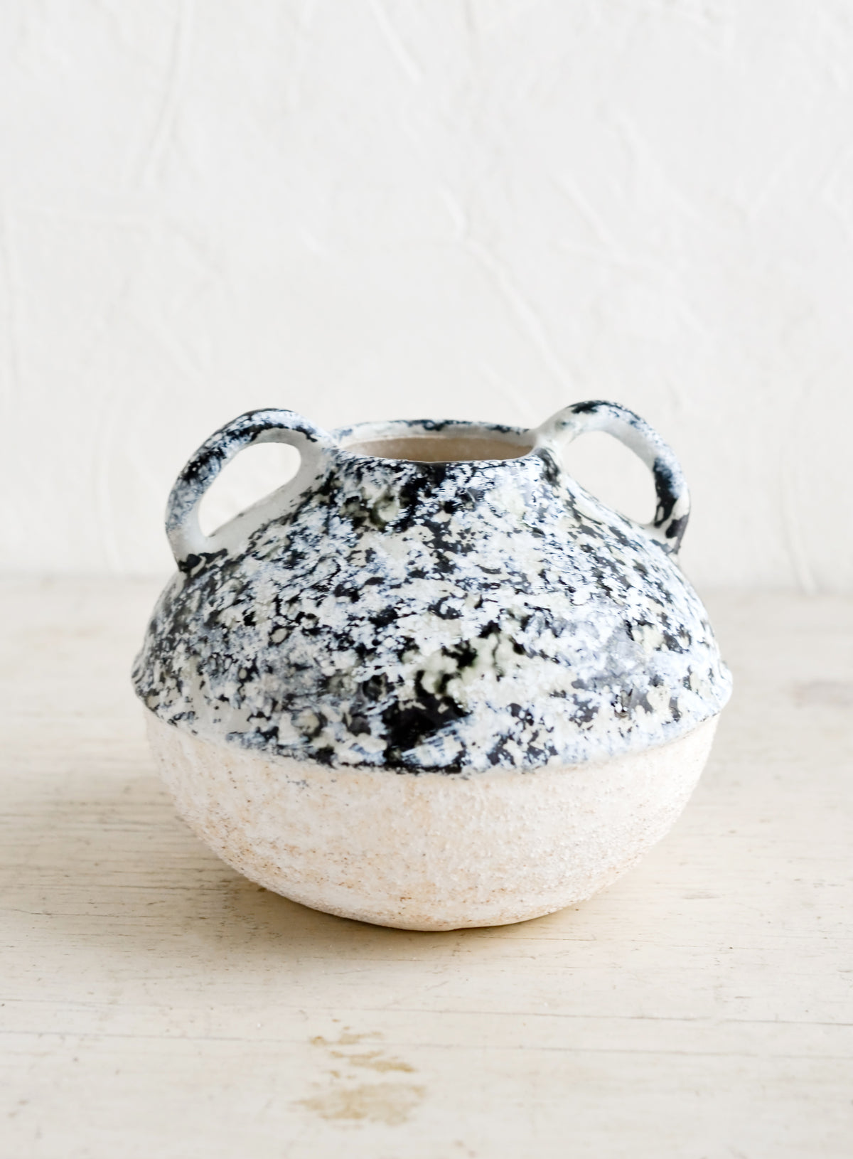 A distressed ceramic vase in short shape with side handles.