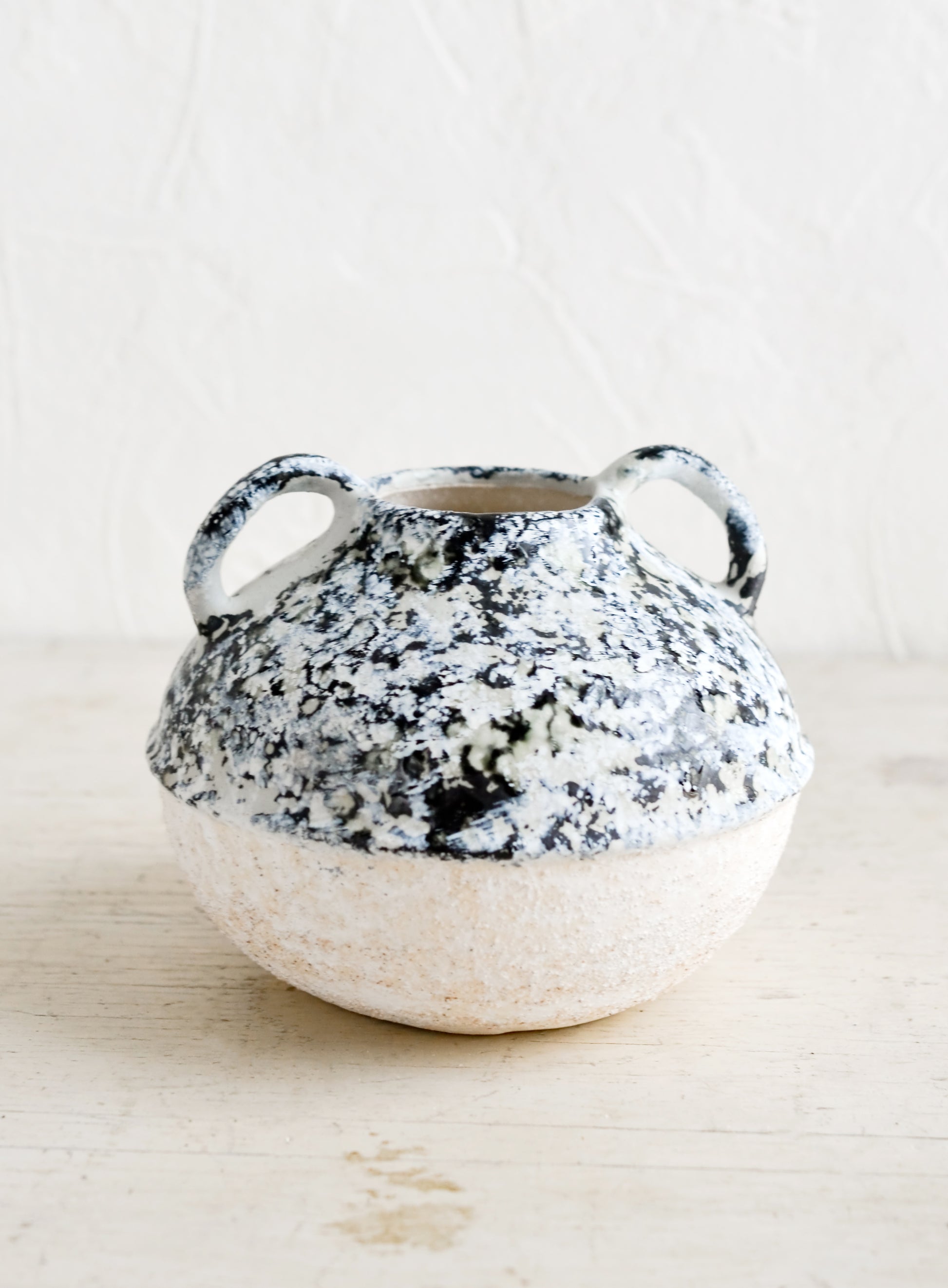 A distressed ceramic vase in short shape with side handles.
