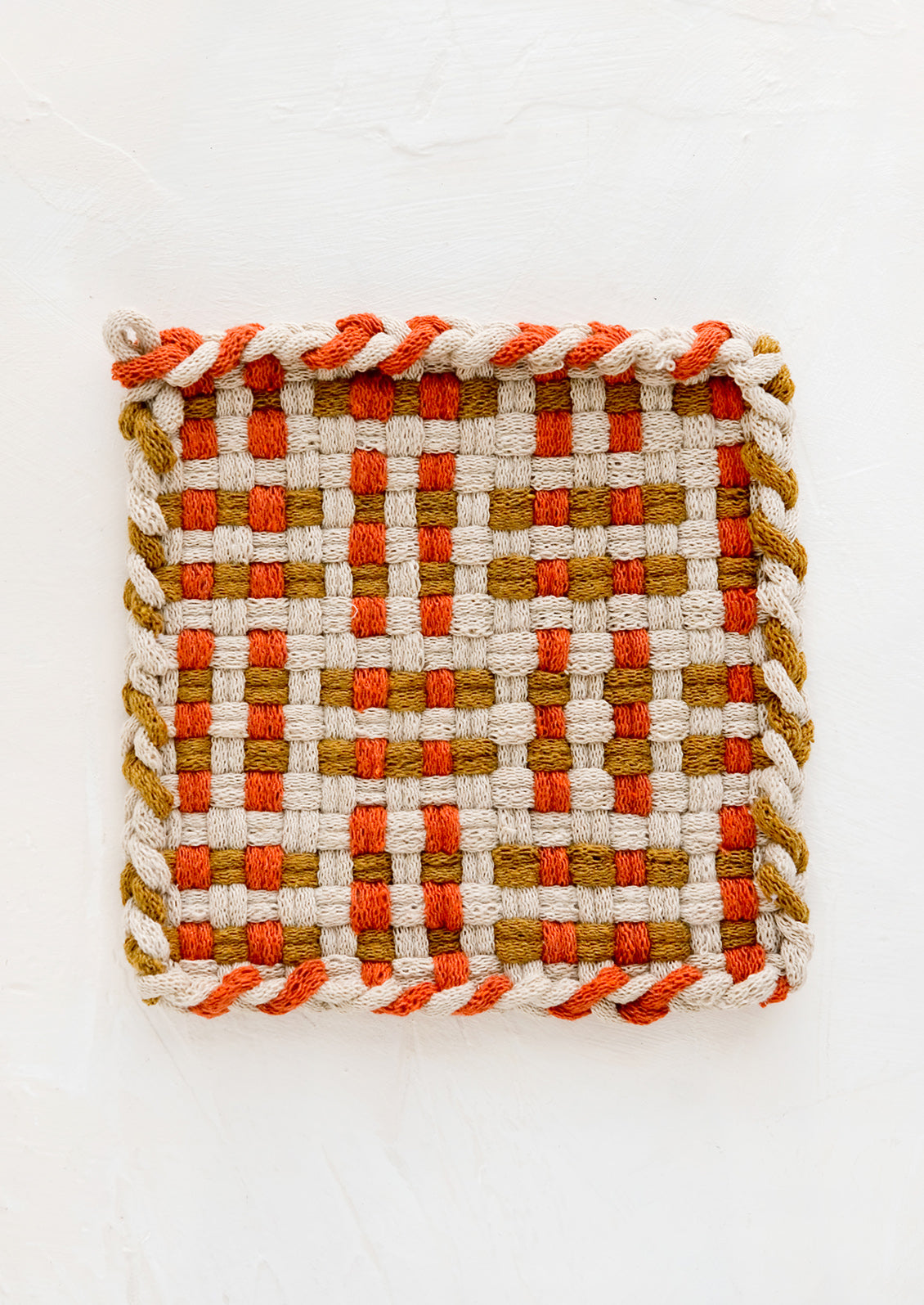 A hand-knit potholder in spice red and ochre woven pattern.