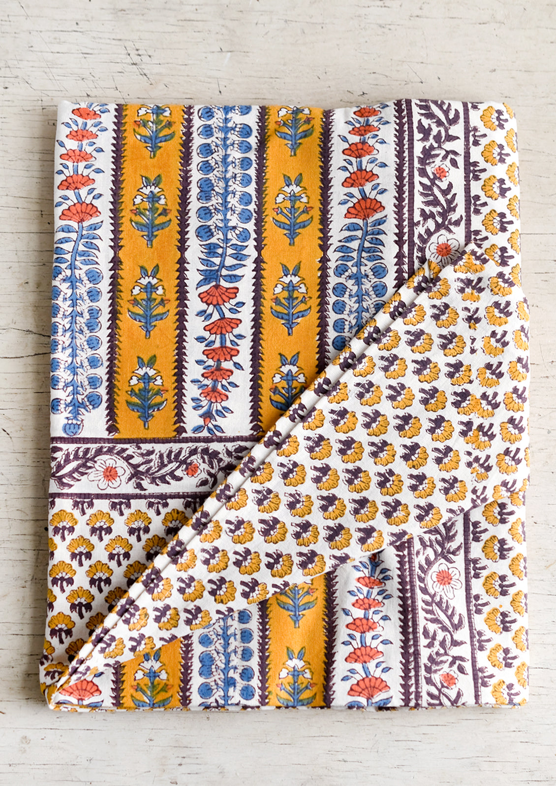 A stripe floral print tablecloth in marigold, purple and blue.