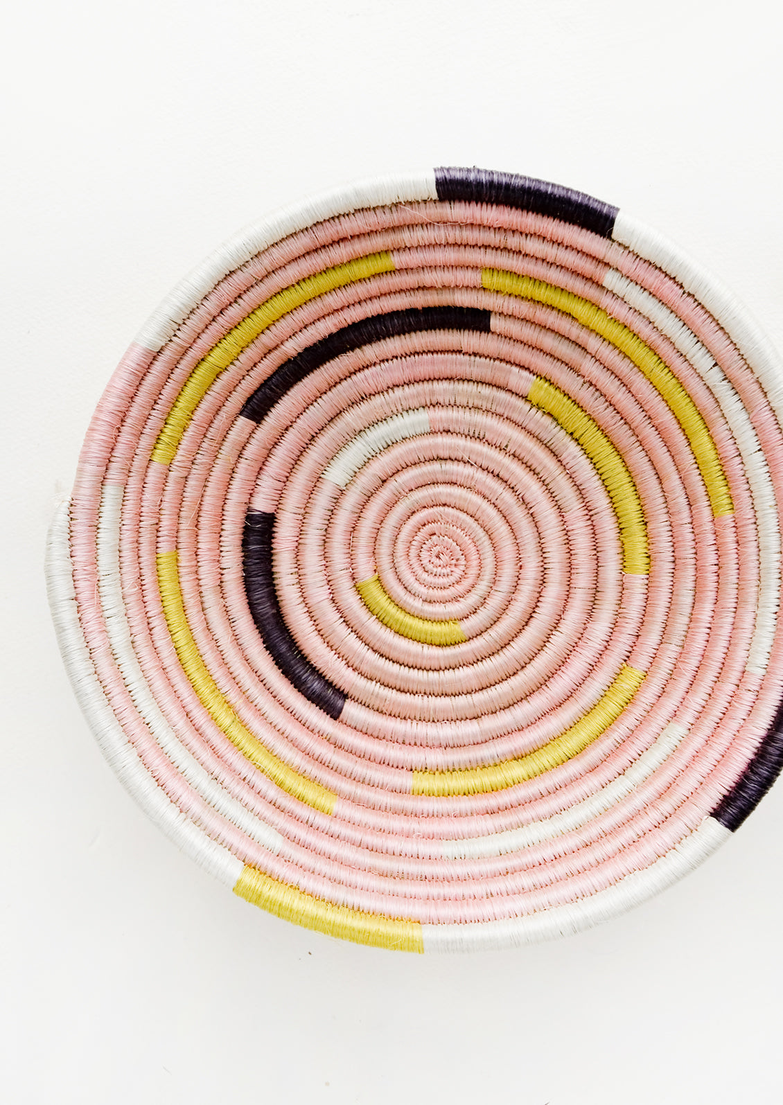 Round bowl made from woven sweetgrass in pink, white, yellow and black modern spiral design.