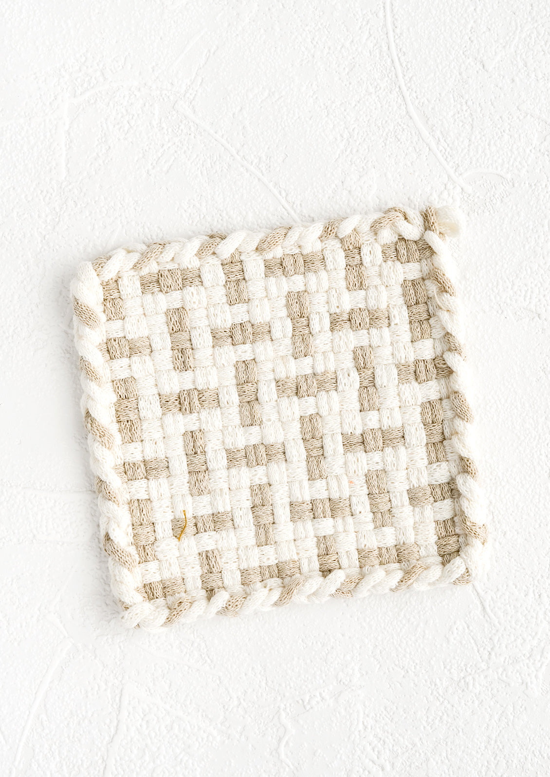 A hand-knit potholder in natural and taupe woven pattern.