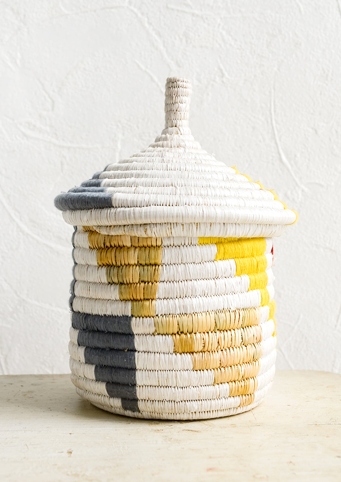 A short woven basket with gourd-style lid in white with natural, yellow and blue-grey triangle pattern.