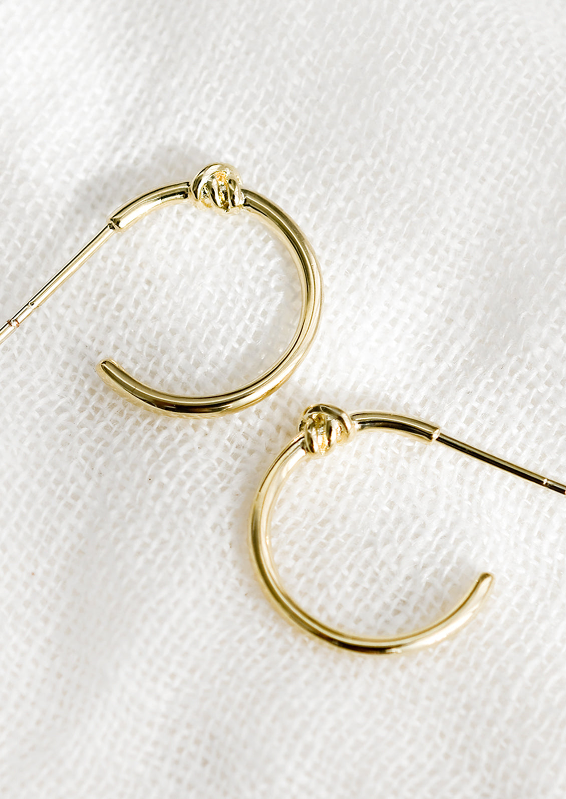 A pair of gold hoop earrings with single knot detail at top.