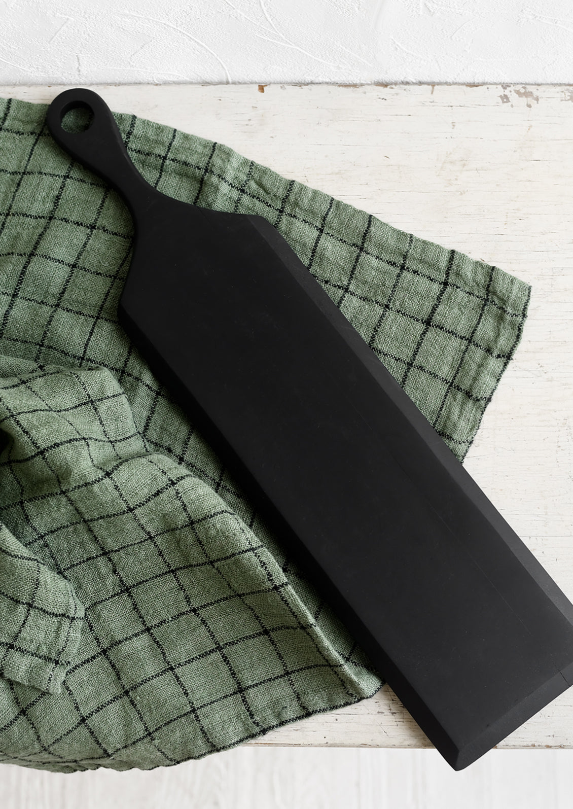 A long and thin paddle-shaped cutting board in black.