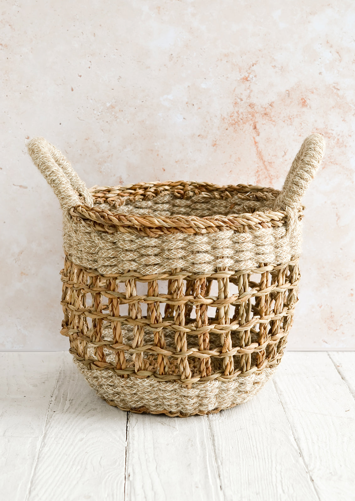 A small open-top round storage basket made from seagrass with braided jute, featuring two handles at top.