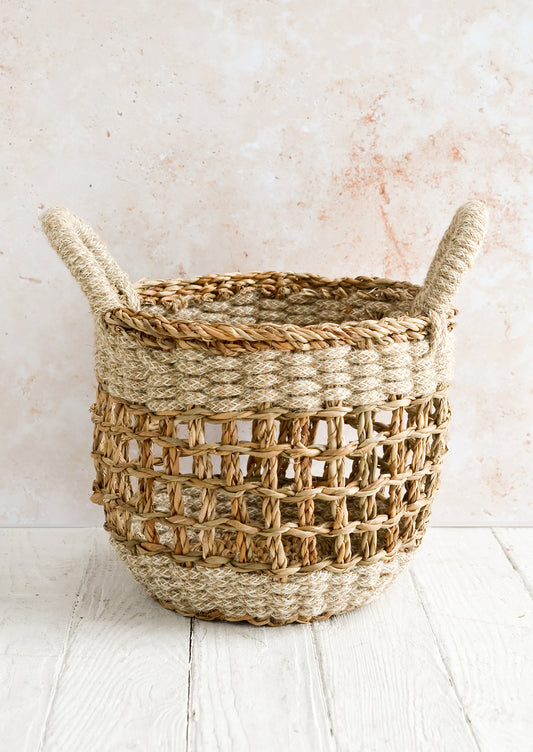 A small open-top round storage basket made from seagrass with braided jute, featuring two handles at top.