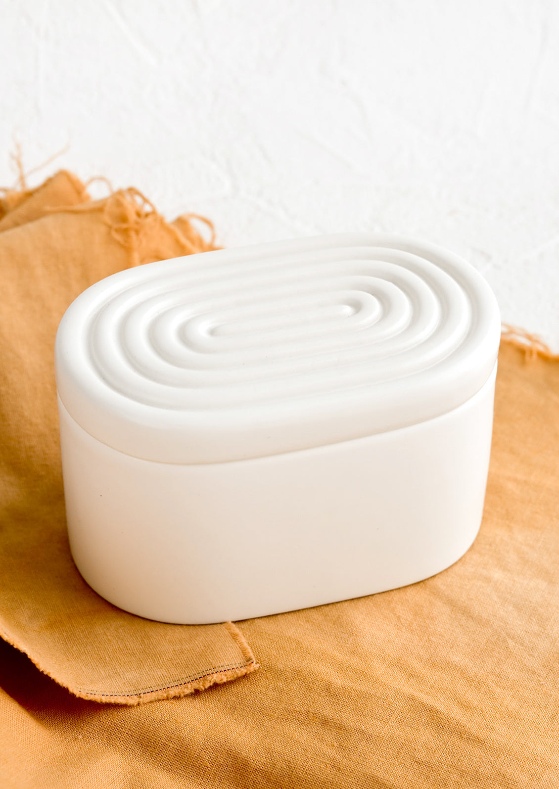 An oval-shaped white ceramic storage box with maze-patterned lid.