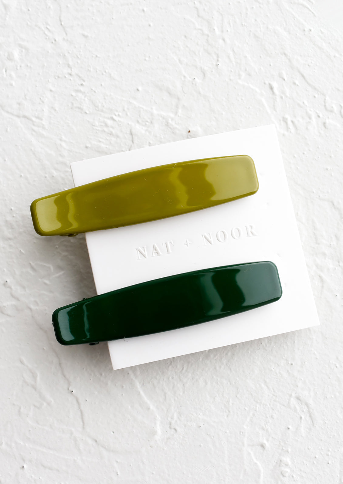 A pair of hair clips with one forest green and one olive green.