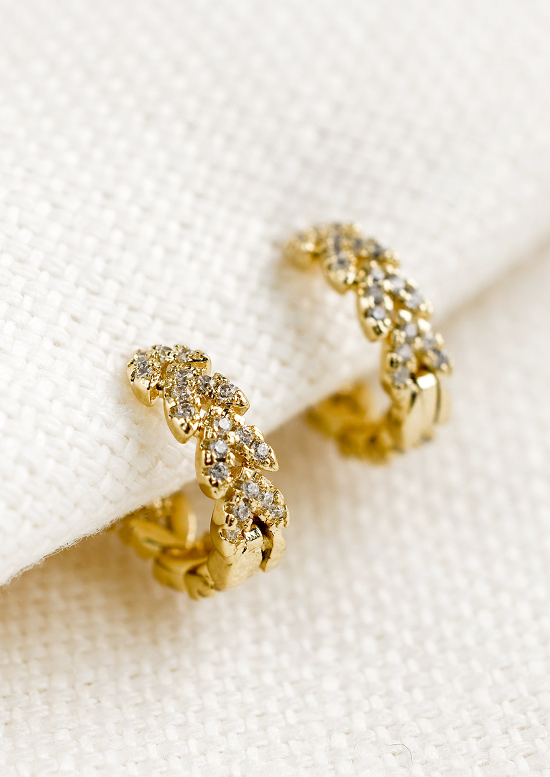 A pair of gold huggie hoop earrings with clear crystal laurel leaf design.