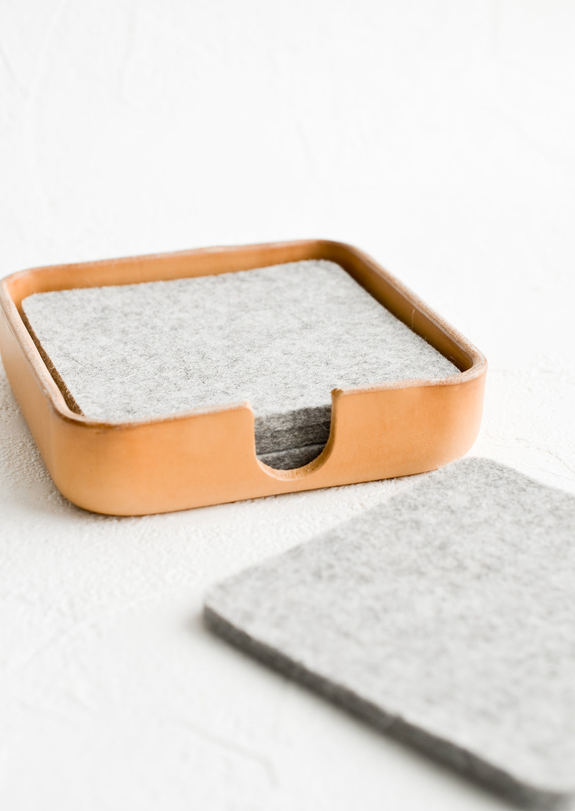 A leather coaster holder containing grey felt coasters.