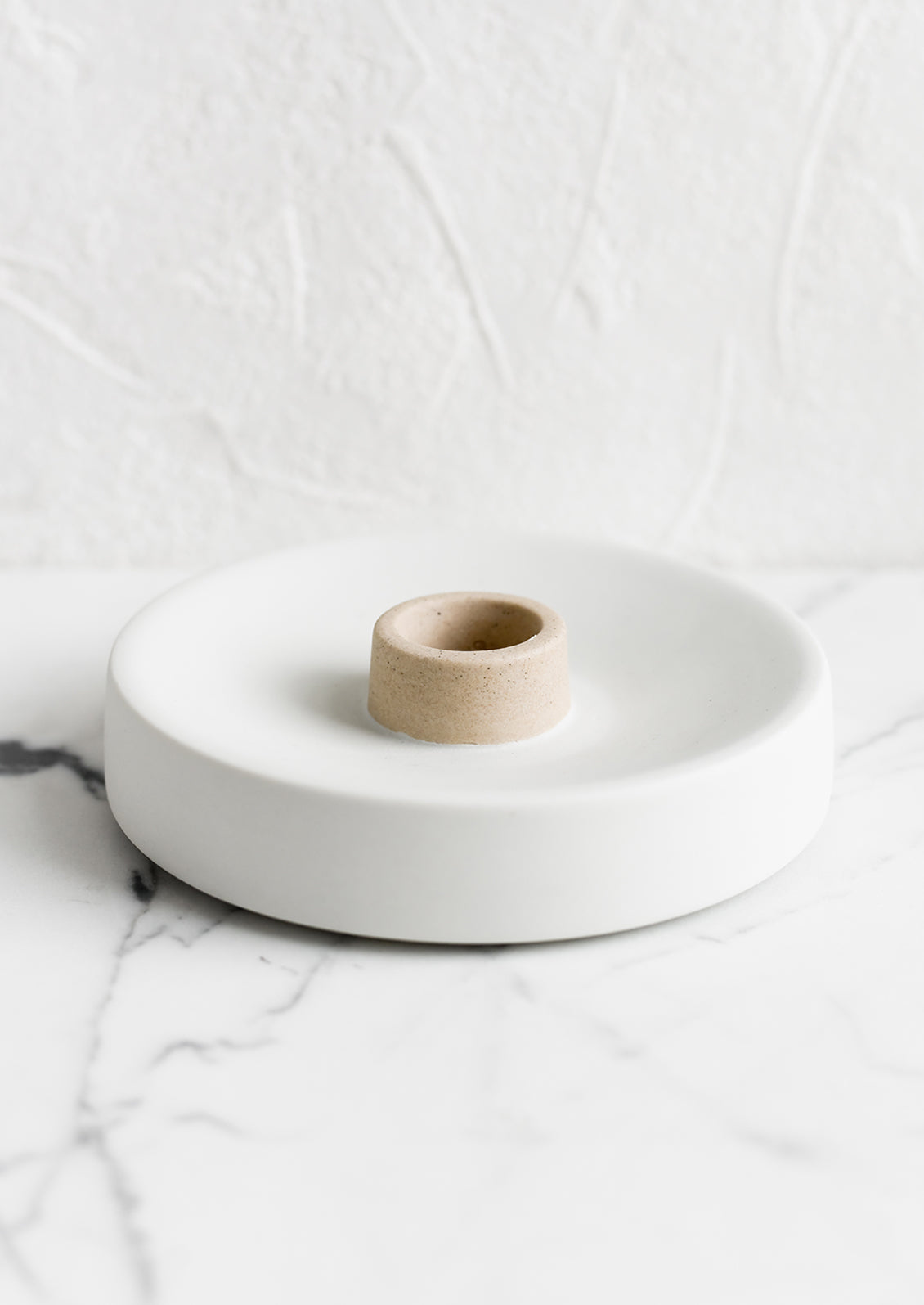 A round ceramic taper candle holder in white and sand.