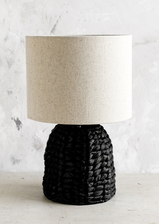 A table lamp with black woven base and linen shade.
