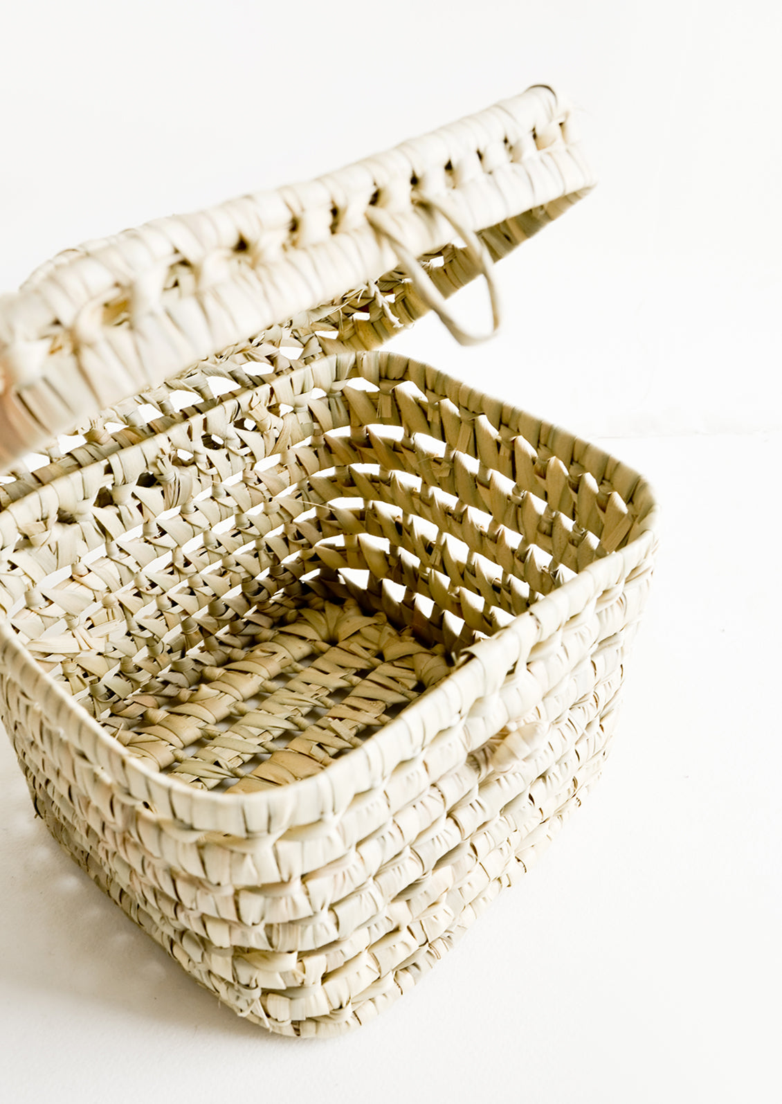 The empty interior of a square, lidded basket woven from natural palm leaf.