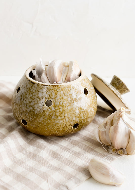 A brown ceramic garlic keeper with garlic heads.