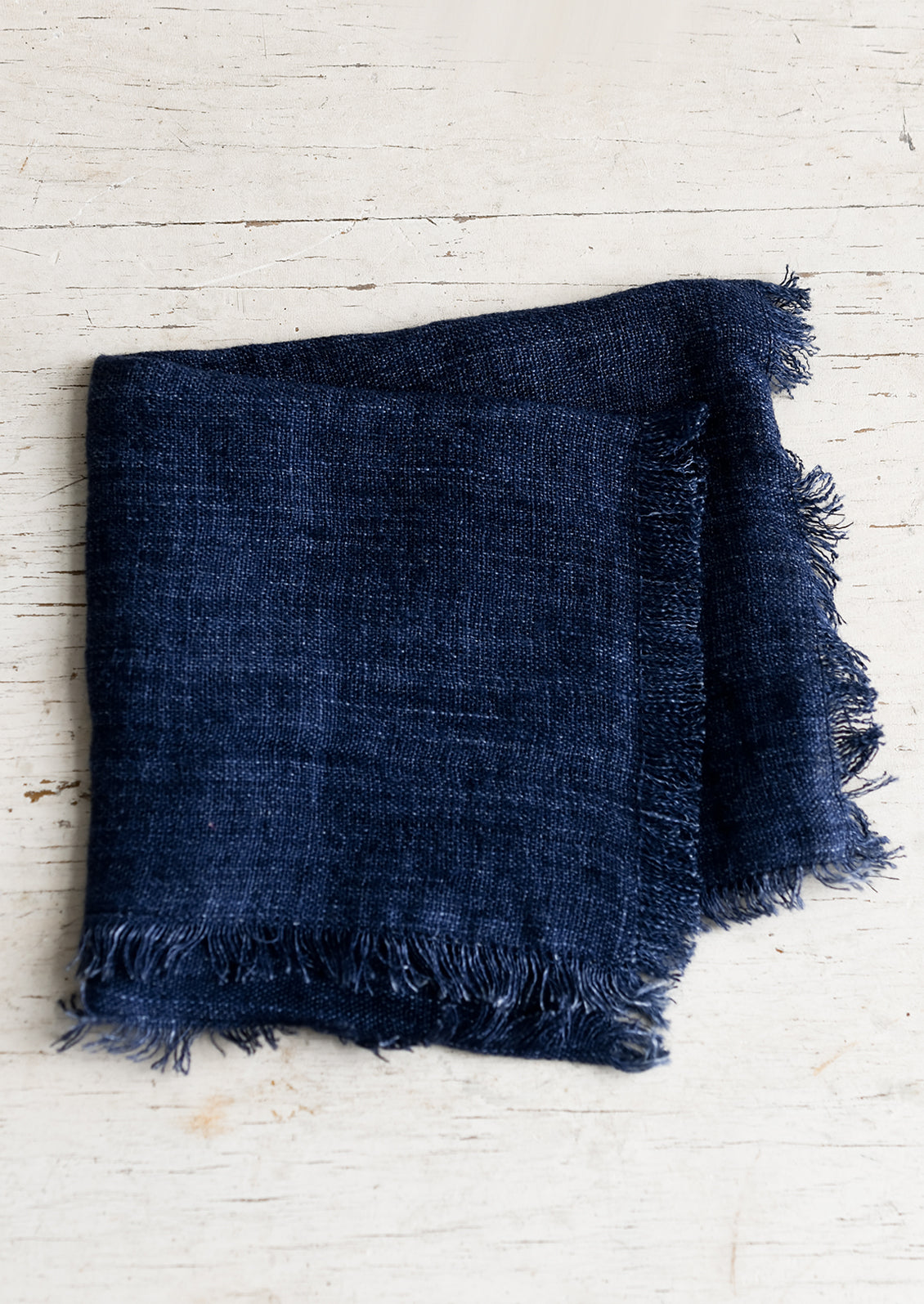 A folded navy blue linen napkin with frayed edges.