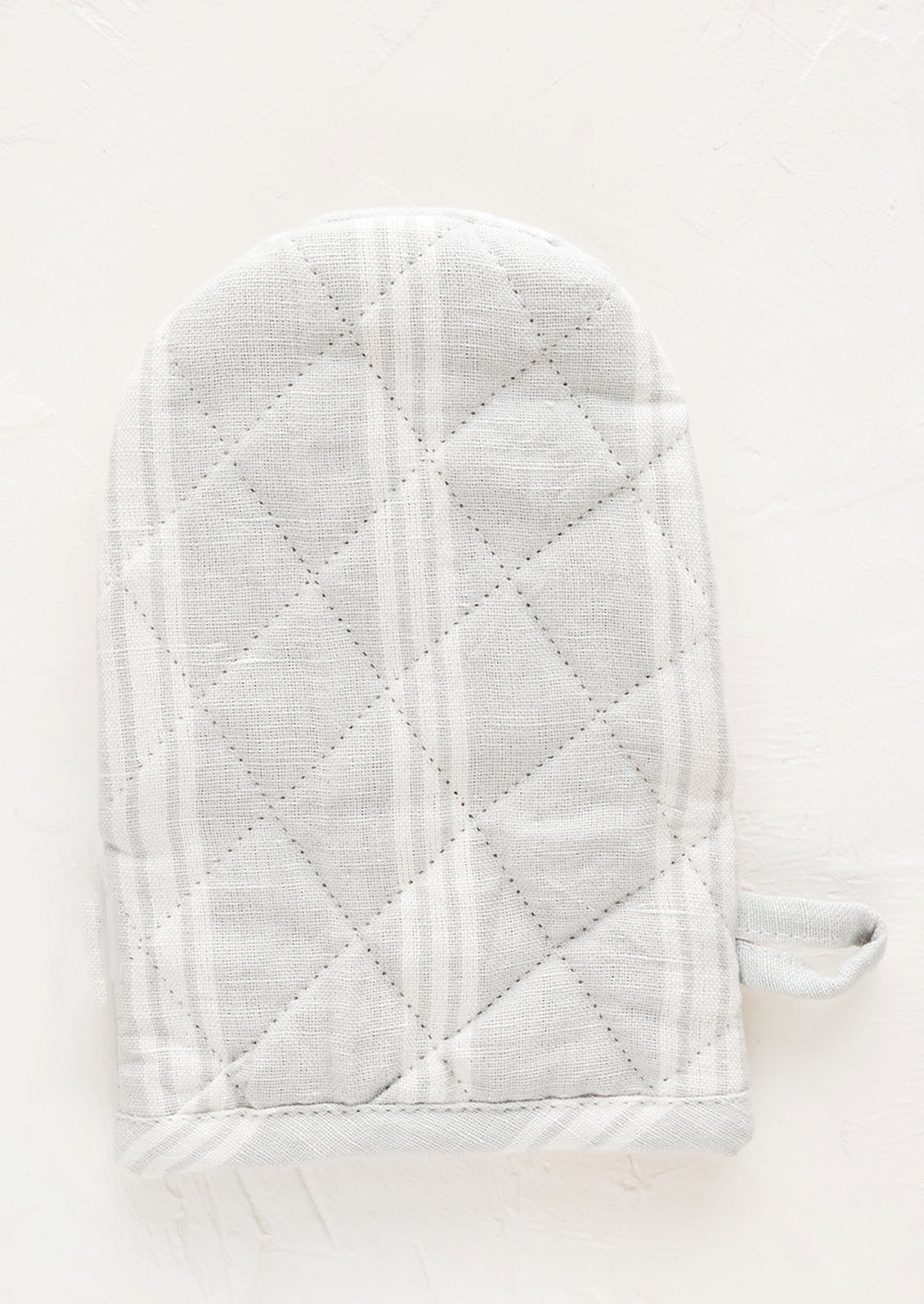 A quilted oven mitt made from light grey and white striped linen.