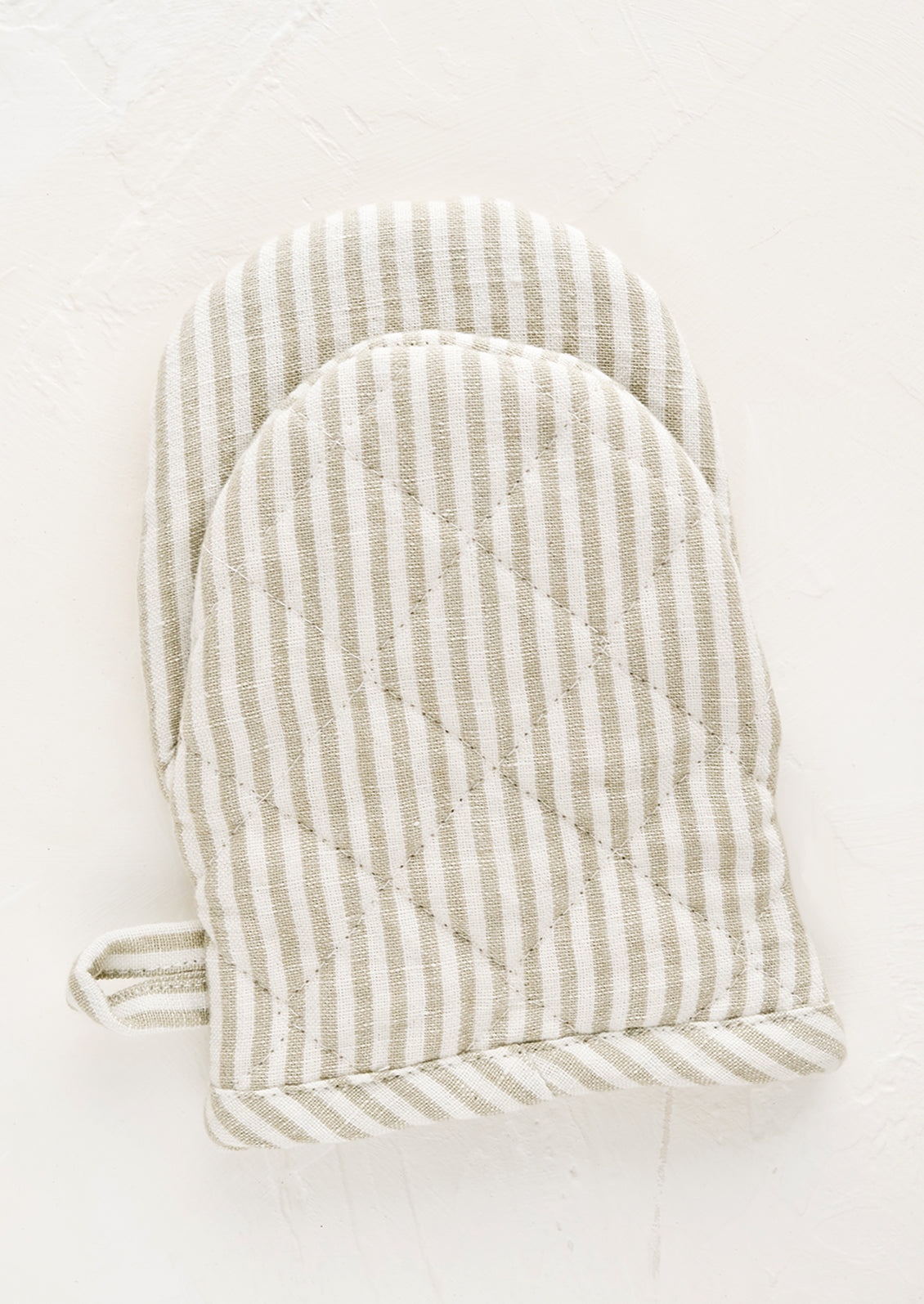 A quilted oven mitt made from tan and ivory striped linen.