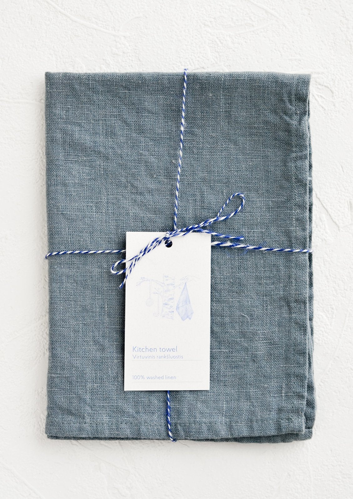 A folded faded blue linen tea towel tied in baker's twine with a decorative hangtag