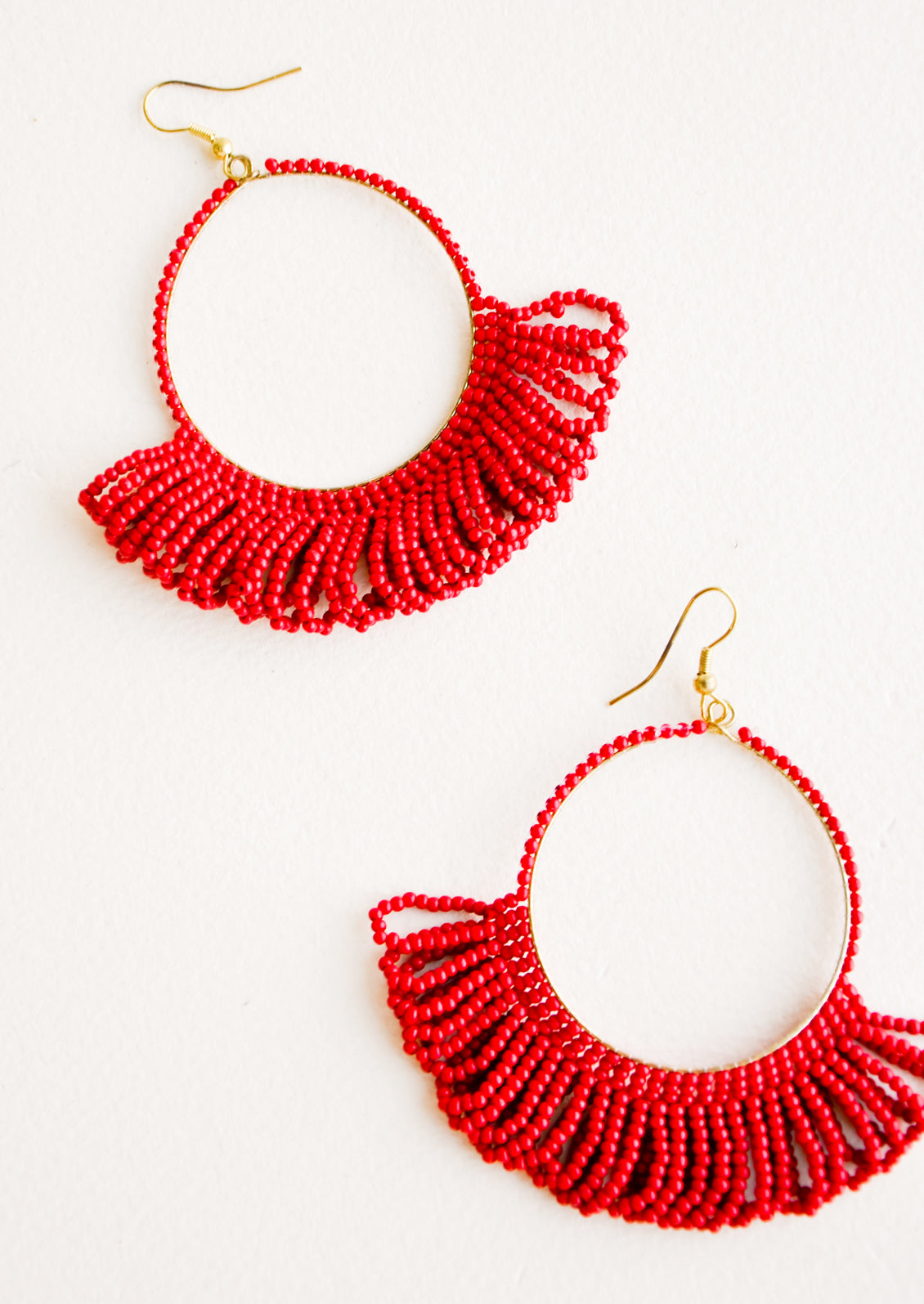 Dangling hoop earrings featuring bright red beads and accented with hanging beaded, looped fringe.