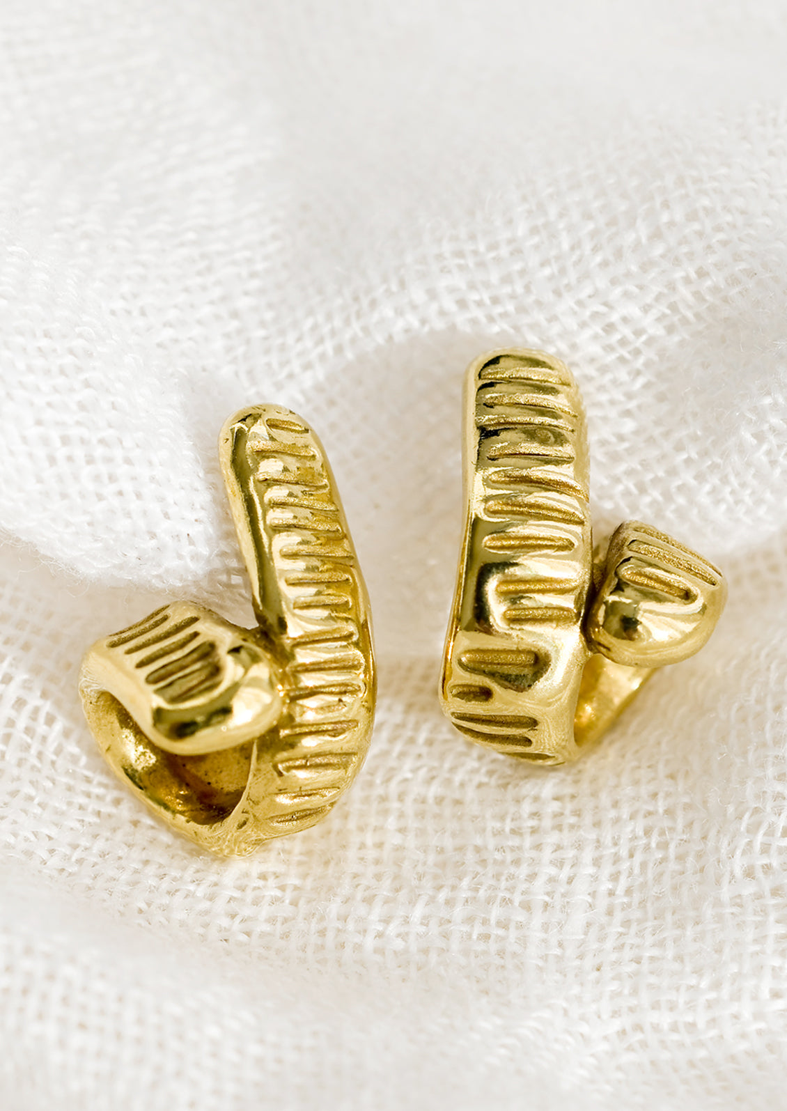 A pair of brass earrings with curled shape and line etched texture.