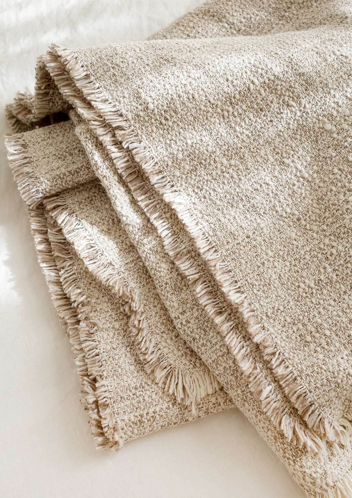A textured boucle blanket with fringe trim in tan/white.