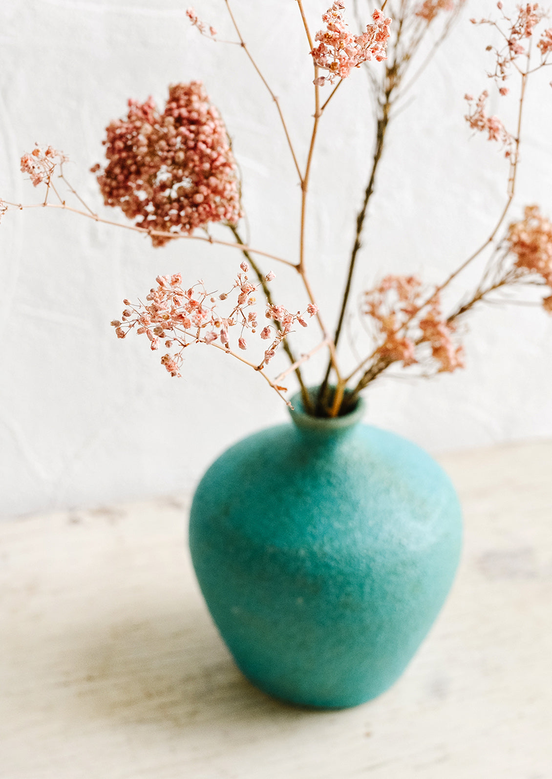 A textured turquoise ceramic vase with dried pink flowers inside.