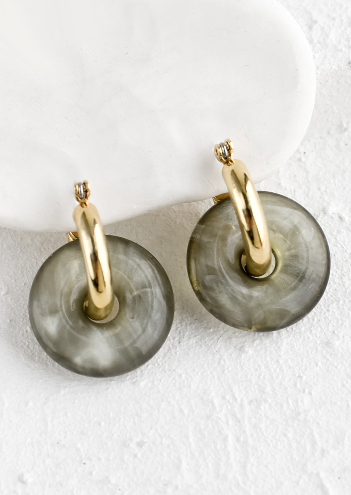 A pair of grey resin donut shaped charms on gold hoop earrings.