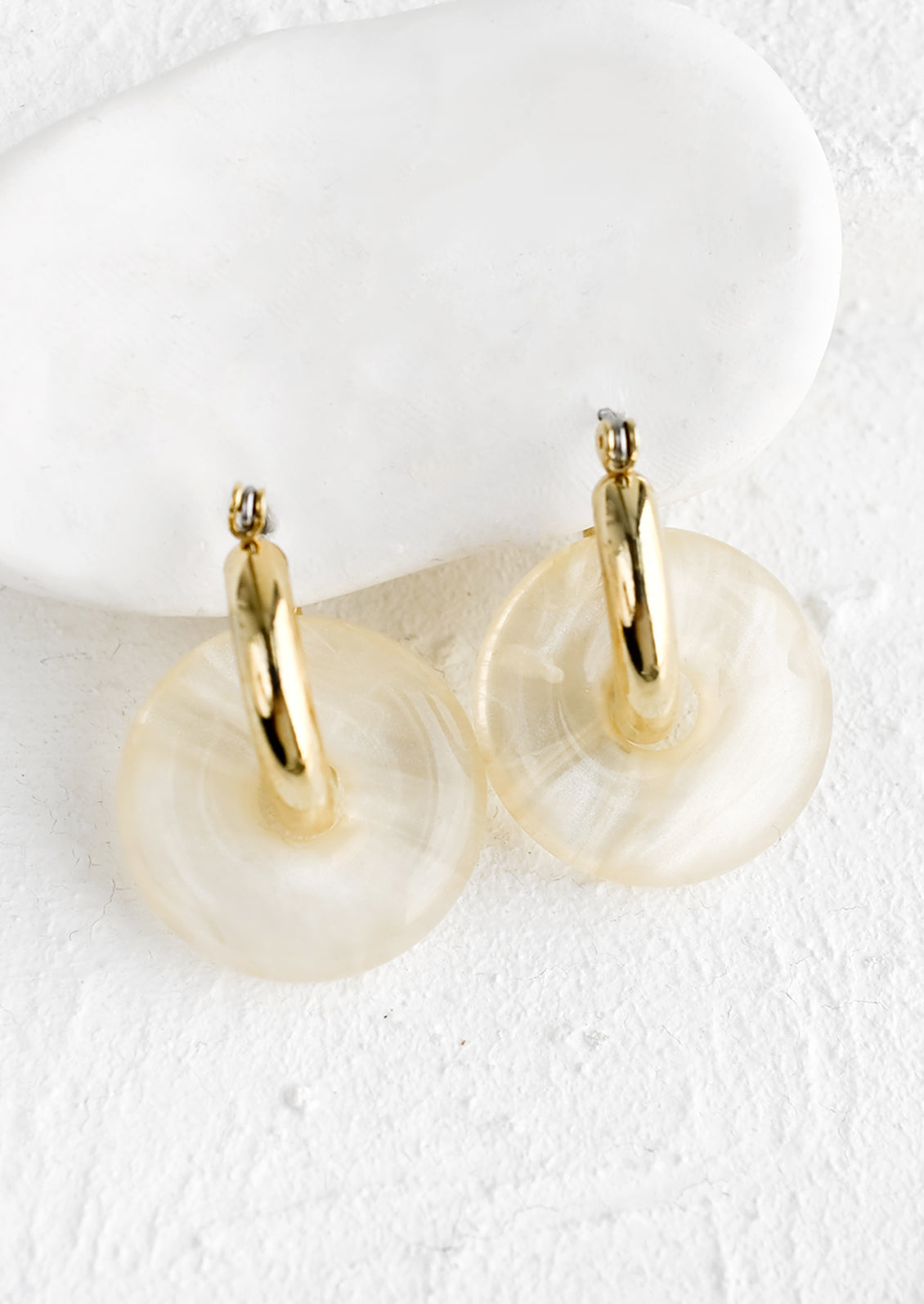 A pair of clear resin donut shaped charms on gold hoop earrings.