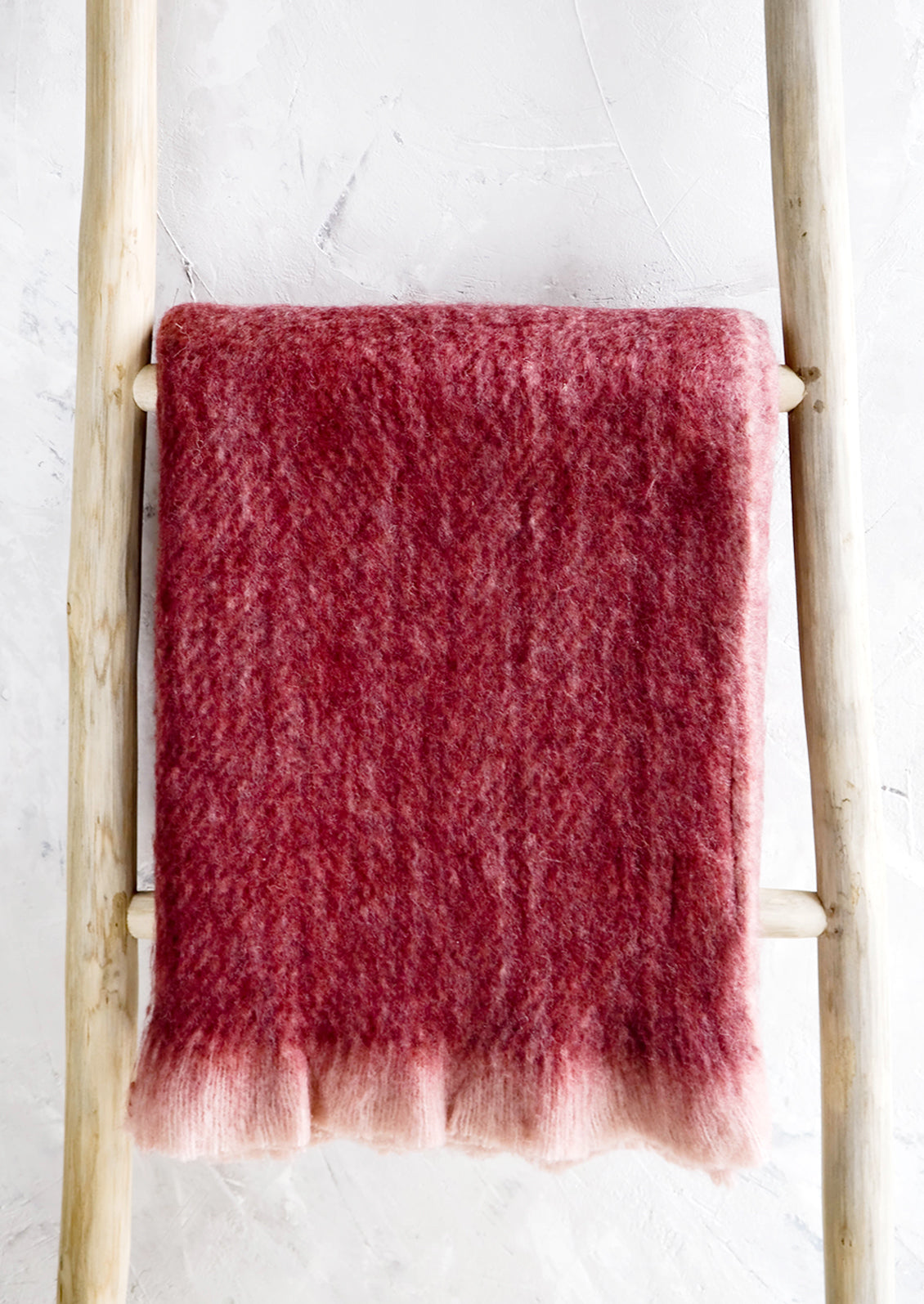 Plush, fuzzy blanket in wine red color with pale pink trim, displayed on ladder