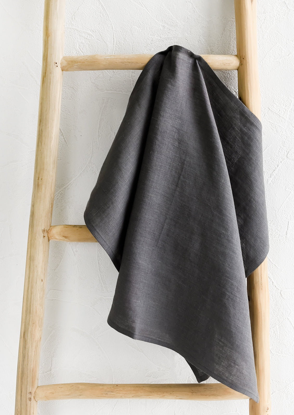 A charcoal linen tea towel draped on a wooden ladder.