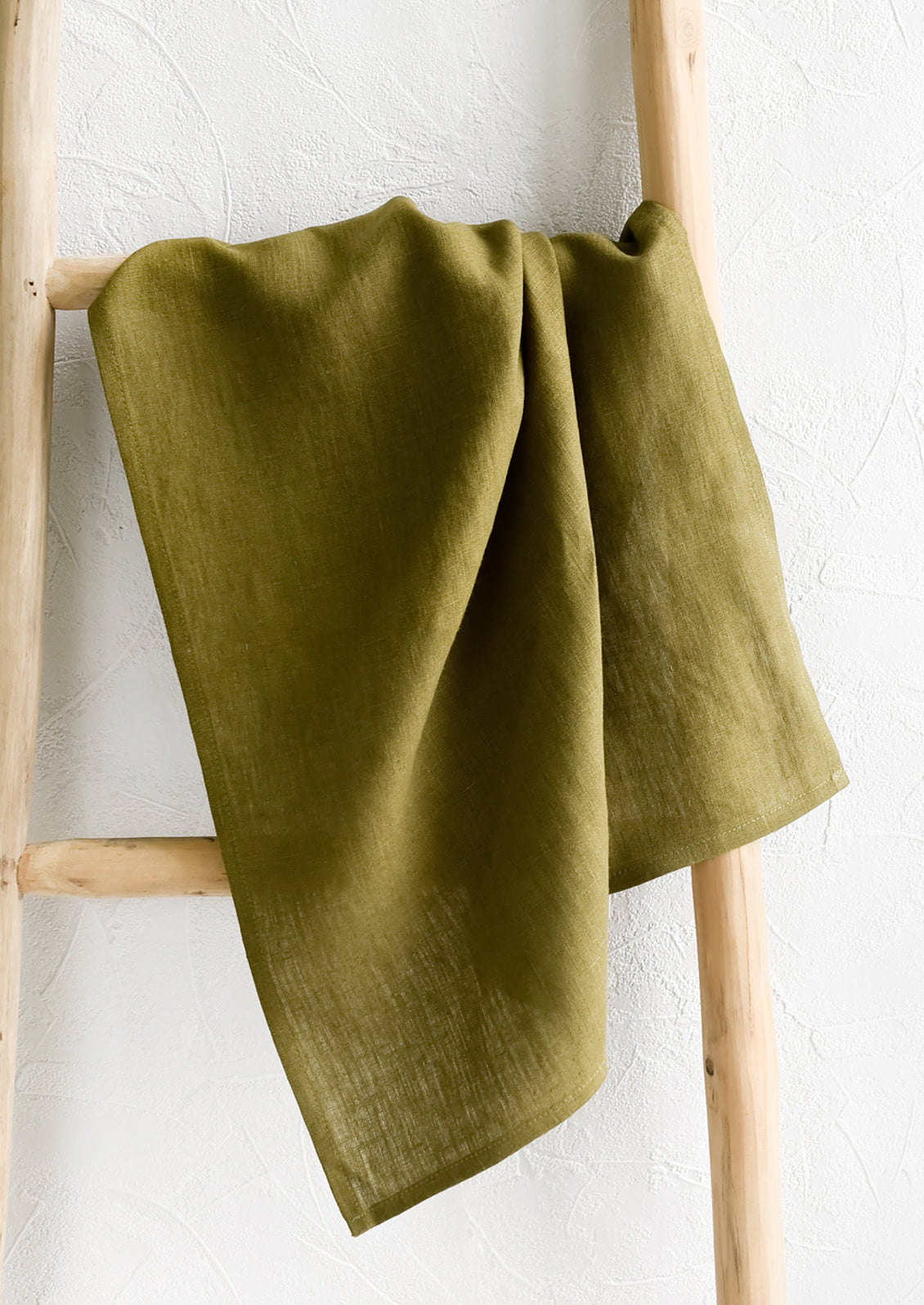 A olive green linen tea towel draped on a wooden ladder.
