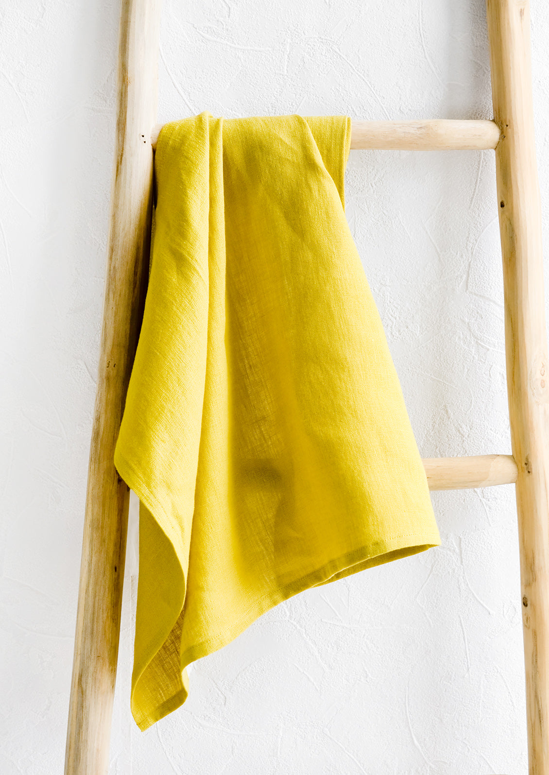 A chatreuse linen tea towel draped on a wooden ladder.