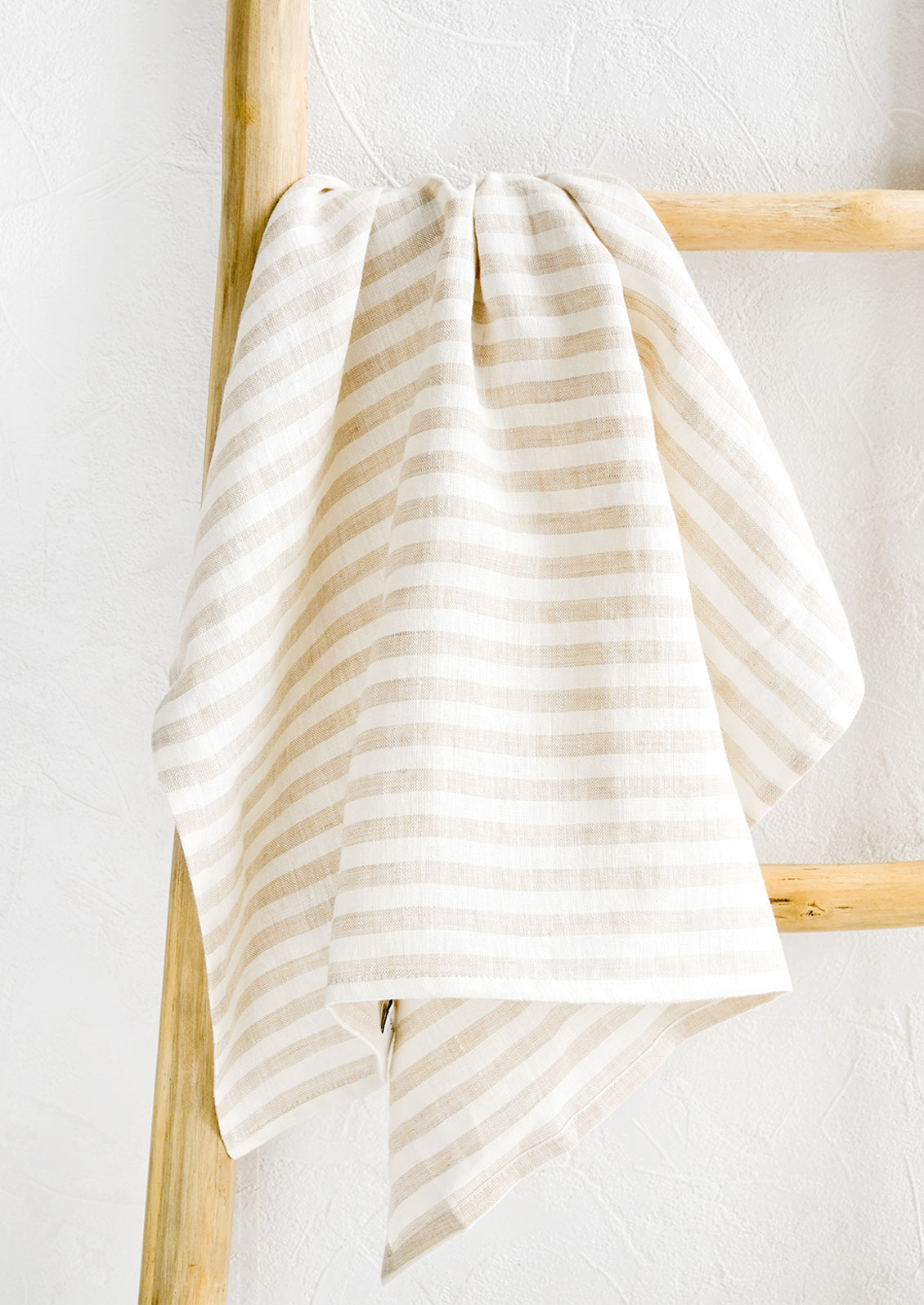 A tan striped linen tea towel draped on a wooden ladder.