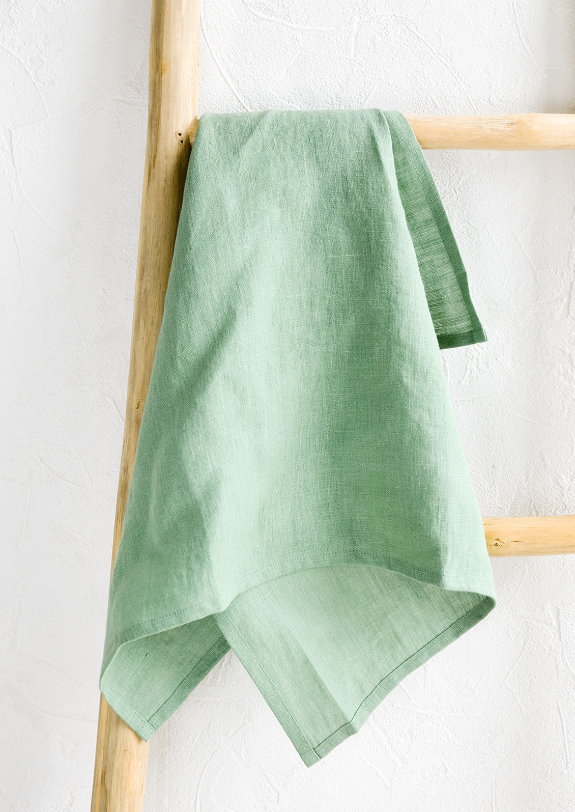 A menthe green linen tea towel draped on a wooden ladder.