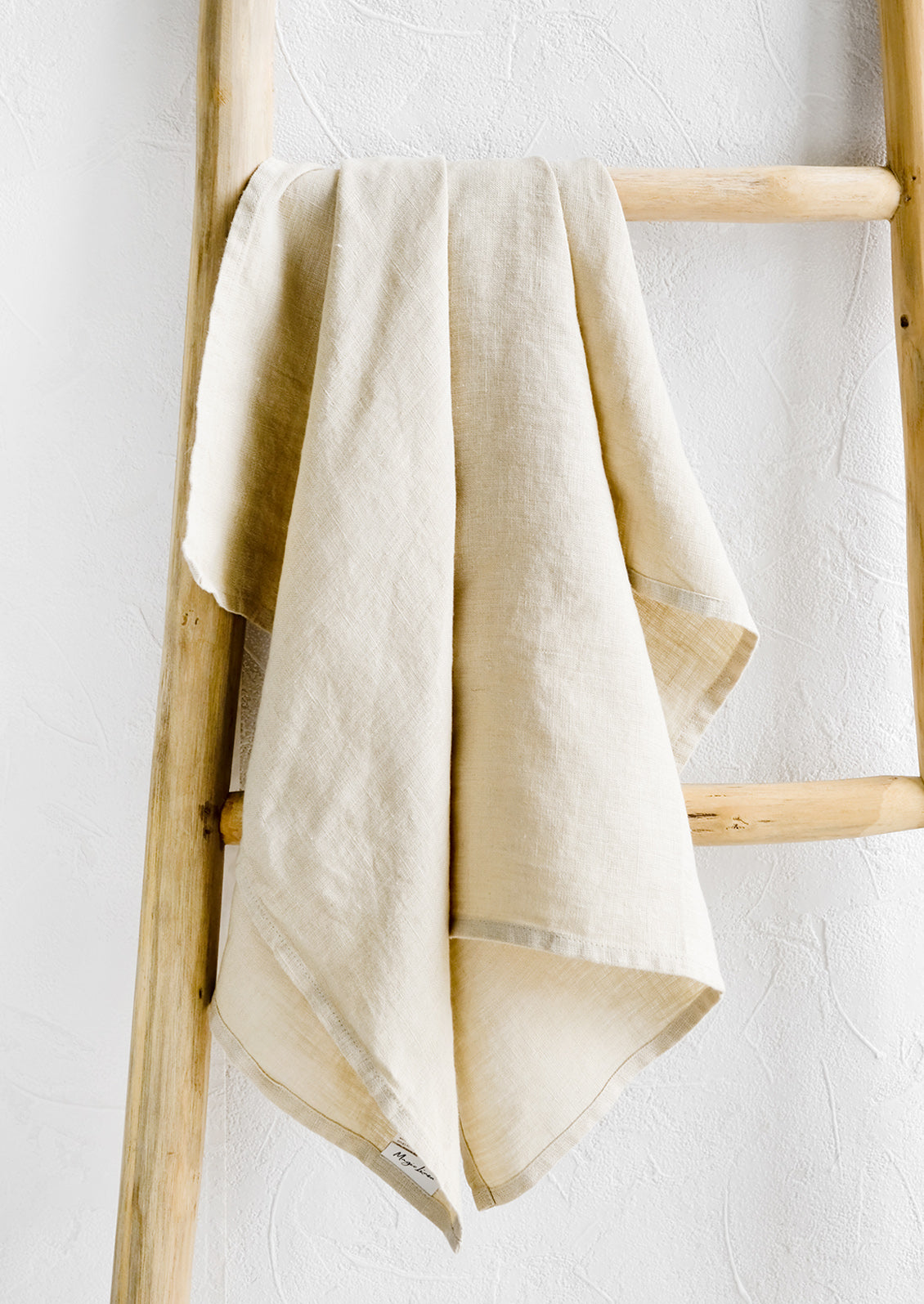 A natural linen tea towel draped on a wooden ladder.