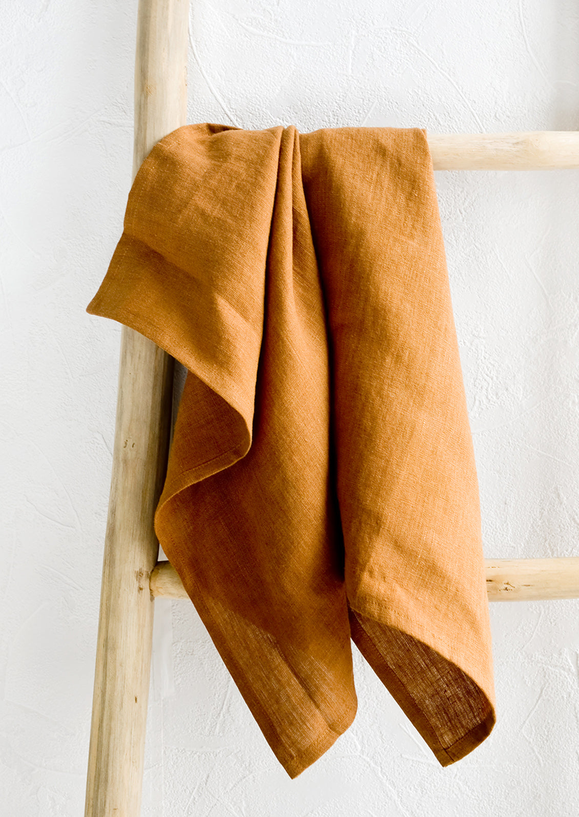 A whiskey brown linen tea towel draped on a wooden ladder.