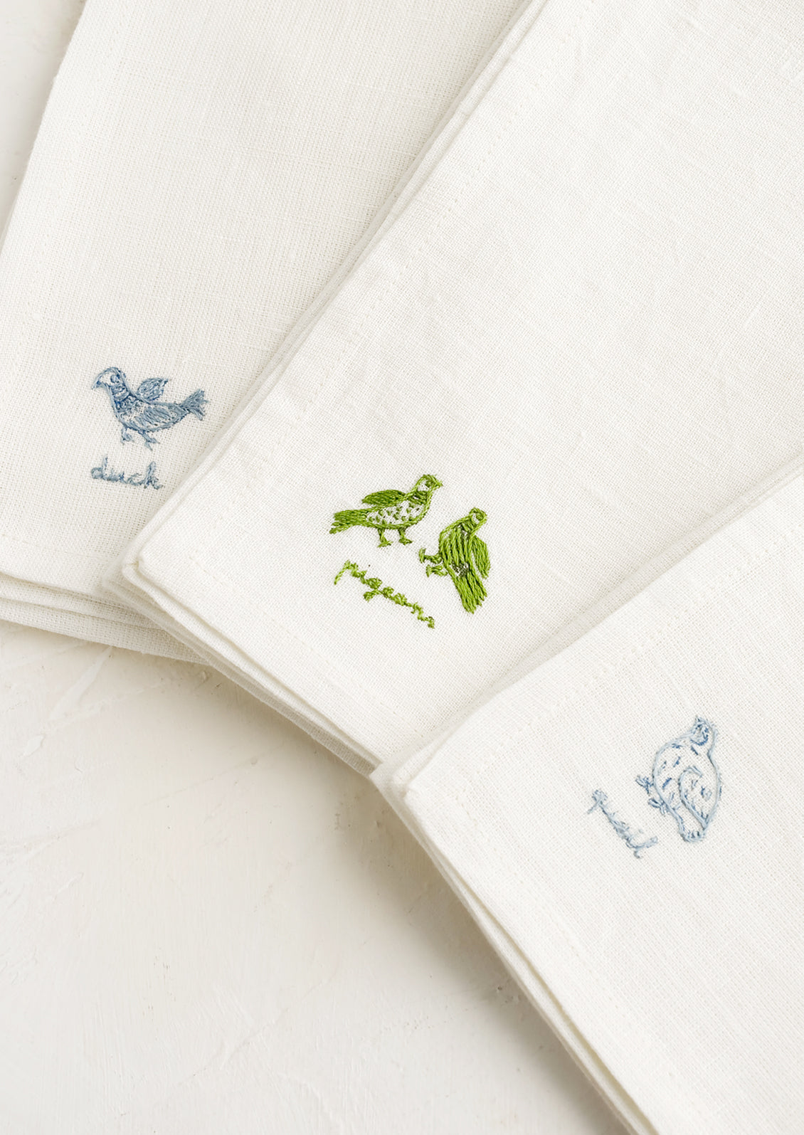 White linen napkins with bird embroidery detailing.