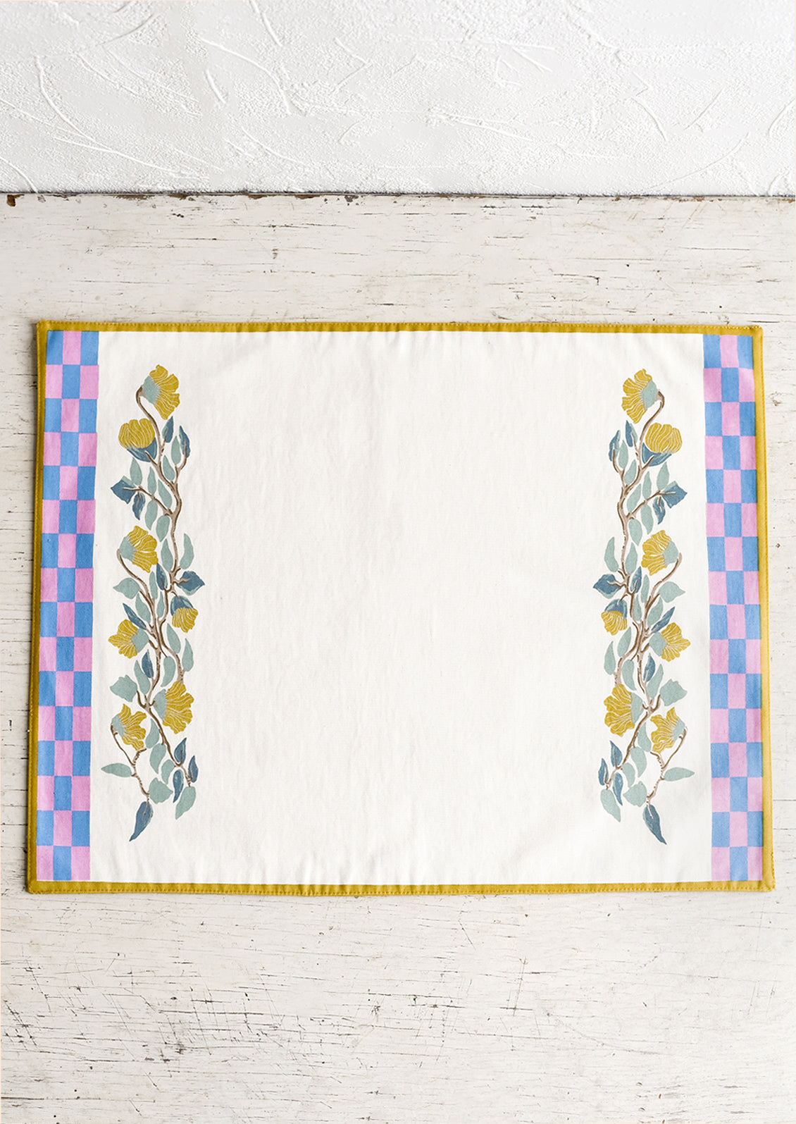 A screenprinted floral placemat with pink and blue checker border.