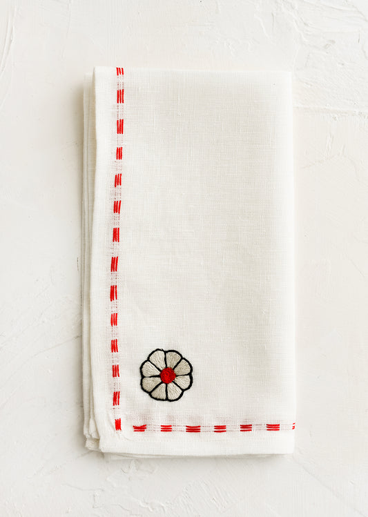 A white linen napkin with embroidery detailing in red.