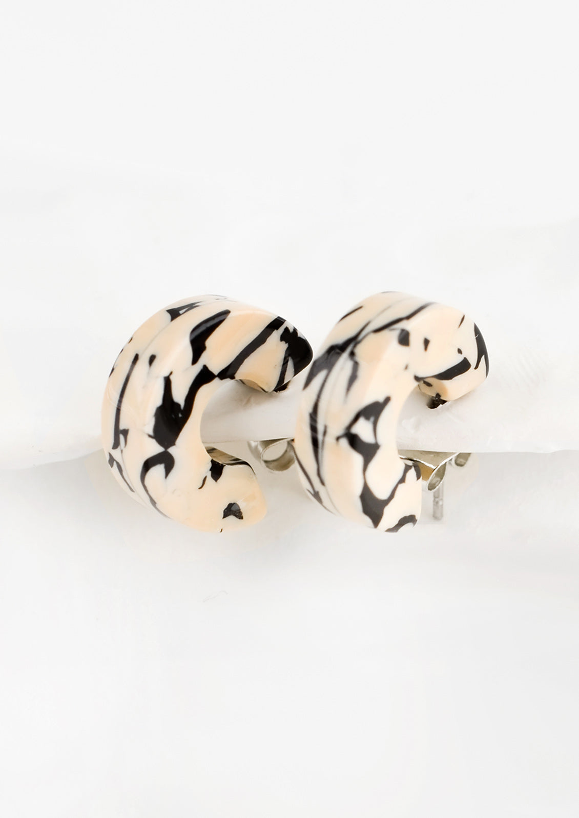A pair of small acetate hoop earrings in tan and black marble.