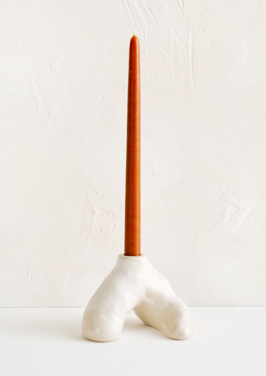 A ceramic taper holder in barnacle-like shape with rust colored taper candle.