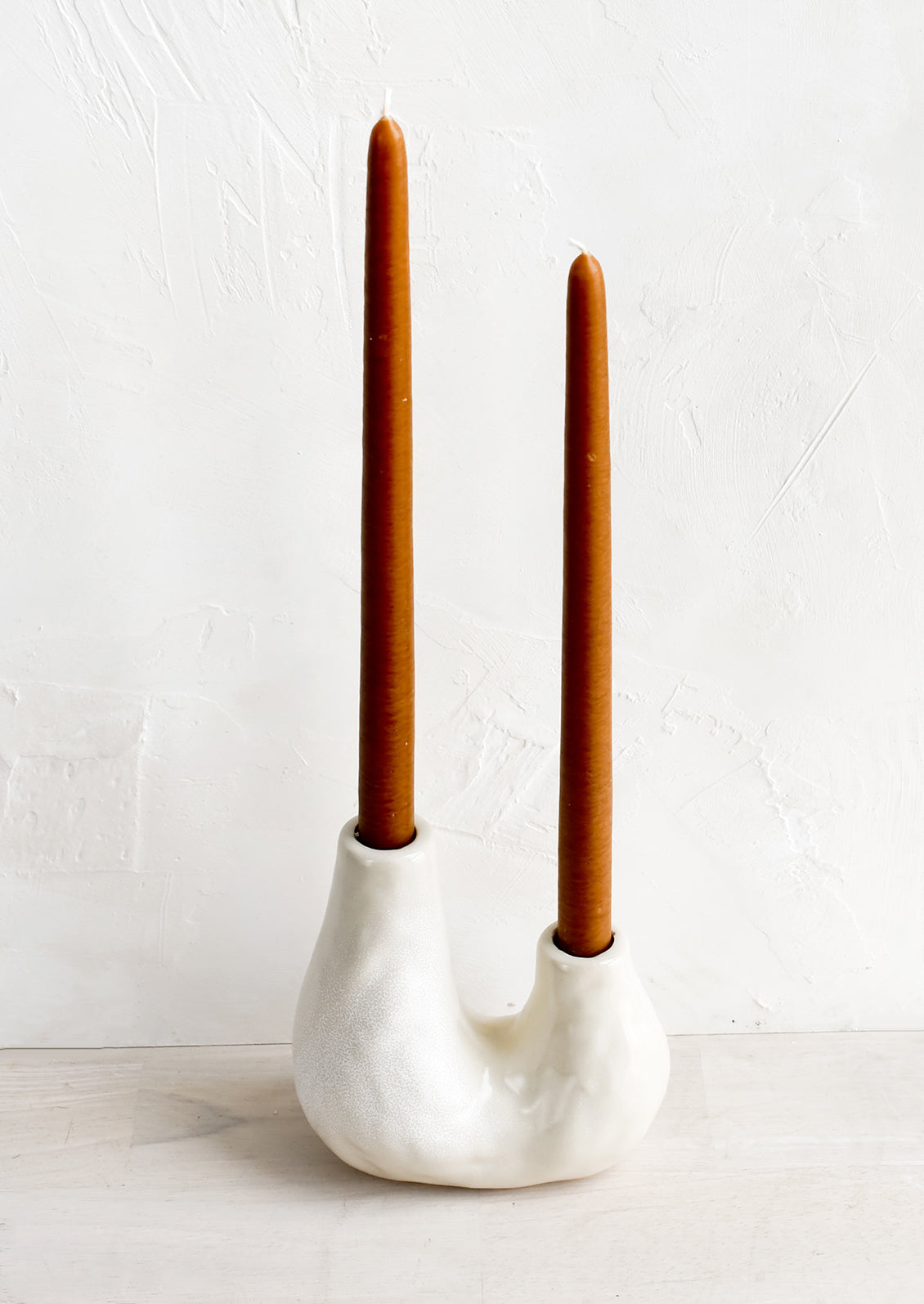 A ceramic 2-taper holder in barnacle-like shape with rust colored taper candle.