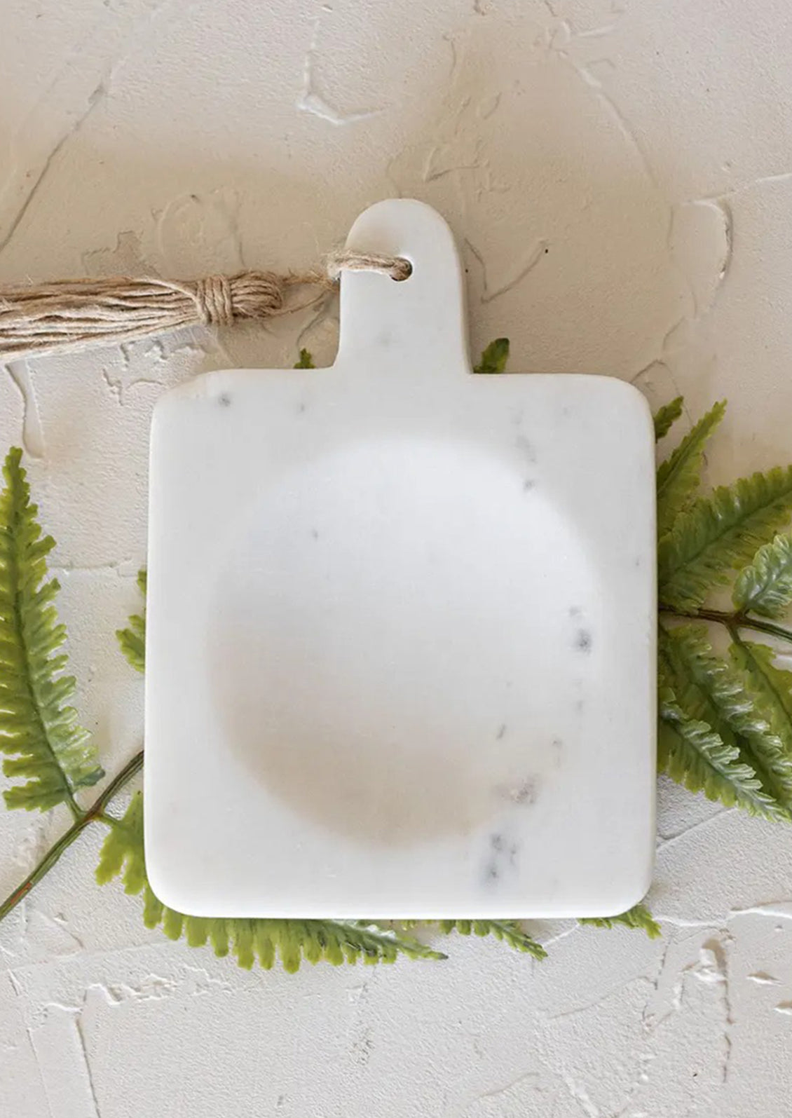 A paddle shaped spoon rest with center well in white marble.