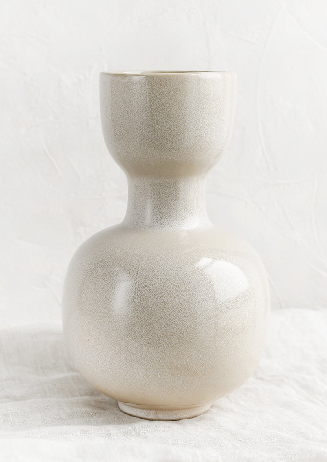 A cream glaze vase with cup shaped top, pinched middle and round bottom.