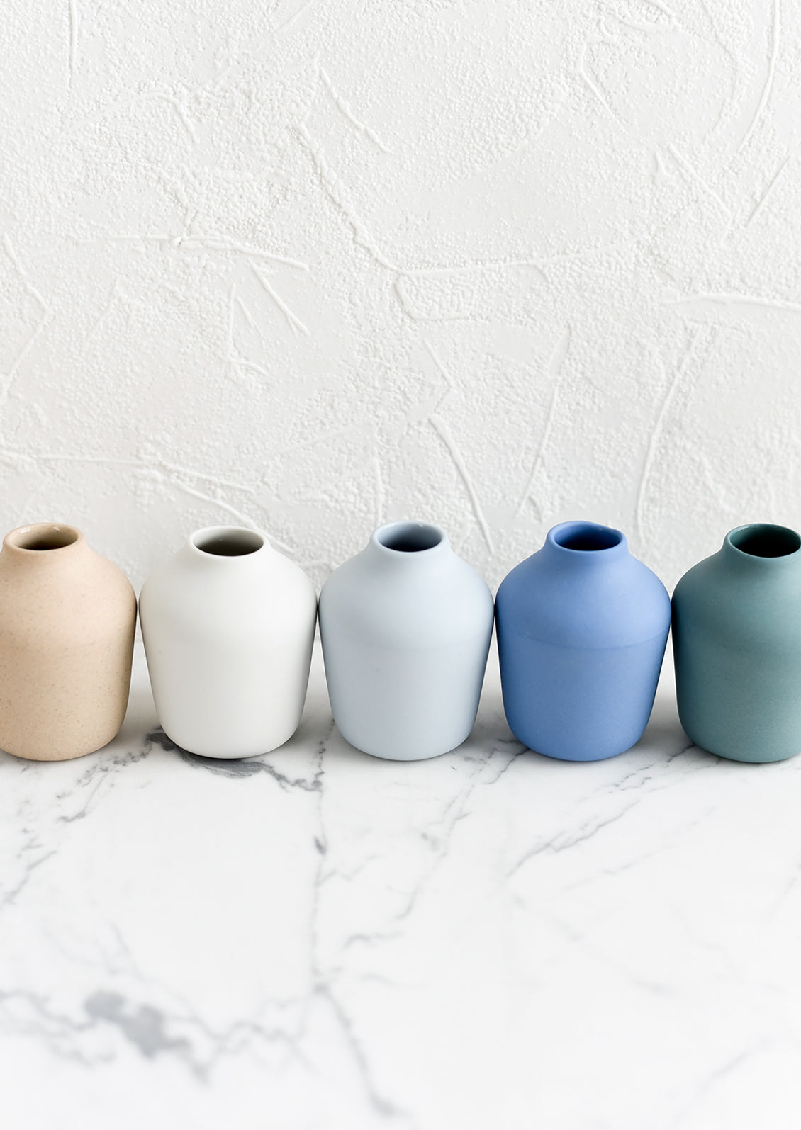 A row of matte porcelain bud vases in different colors.