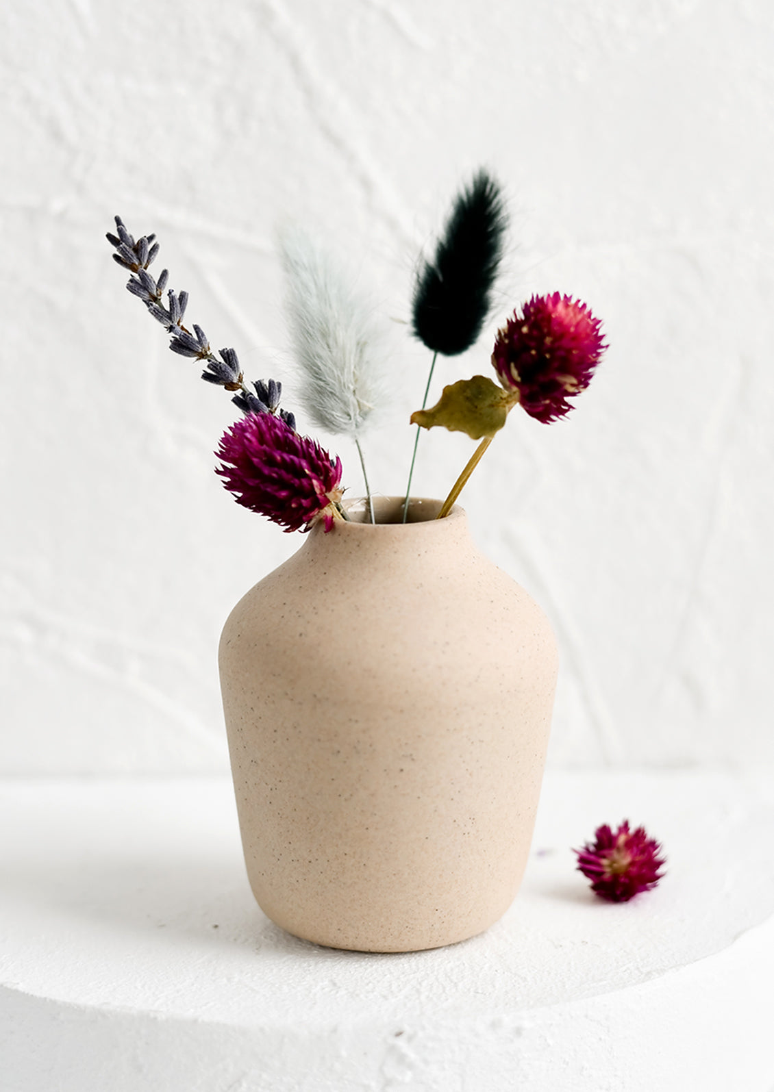 A sand colored porcelain bud vase with dried flowers.