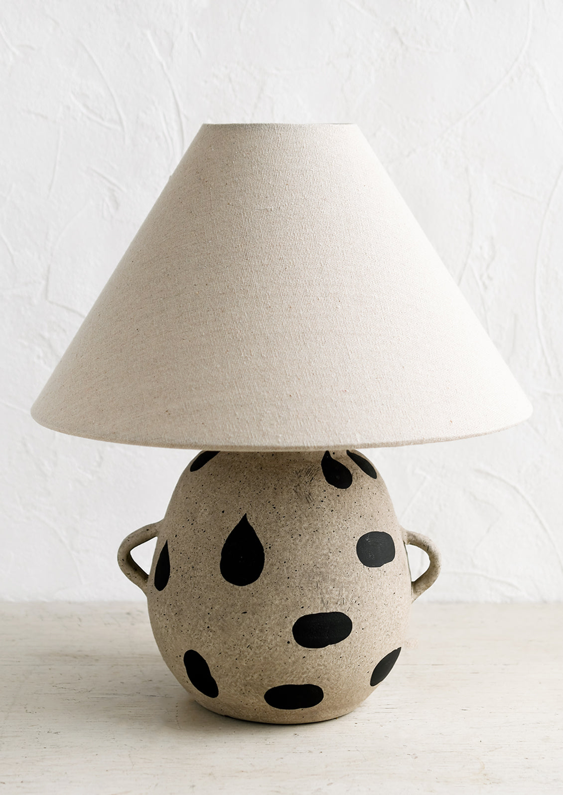 A ceramic table lamp with dot print and side handles on base, with tapered linen shade.